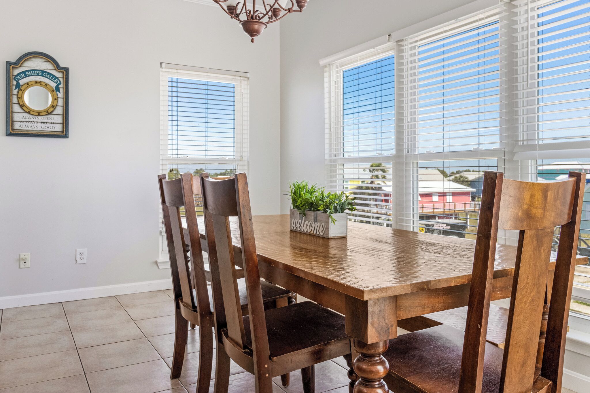 A dining area with a wooden table and chairs, a welcome planter, and a ship's gallery sign.