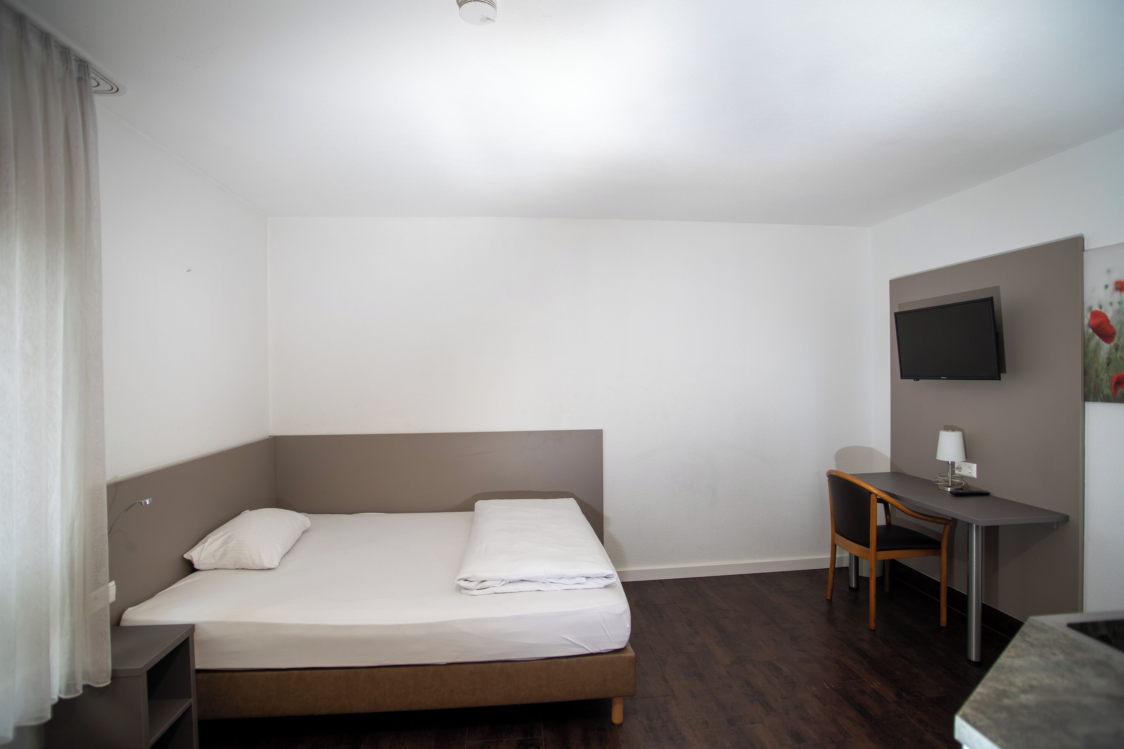 A hotel room with a bed, a desk, a chair, a TV, and a painting on the wall.