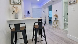 A modern kitchen with two bar stools, a white countertop, and a ceiling with recessed lighting. - Blue Wave Retreat (Beach) (Daytona Beach)