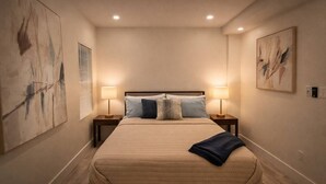 A bedroom with a bed, two bedside lamps, a nightstand, and two abstract paintings on the walls. - Blue Wave Retreat (Beach) (Daytona Beach)