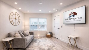 A modern living room with a grey sofa, a large wall clock, and a framed logo on the wall. - Blue Wave Retreat (Beach) (Daytona Beach)