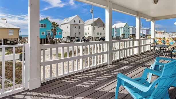 A wooden deck with white railings, blue chairs, and a view of colorful houses by the beach. - Bikini Bottom by Southern Vacation Rentals (Gulf Shores)