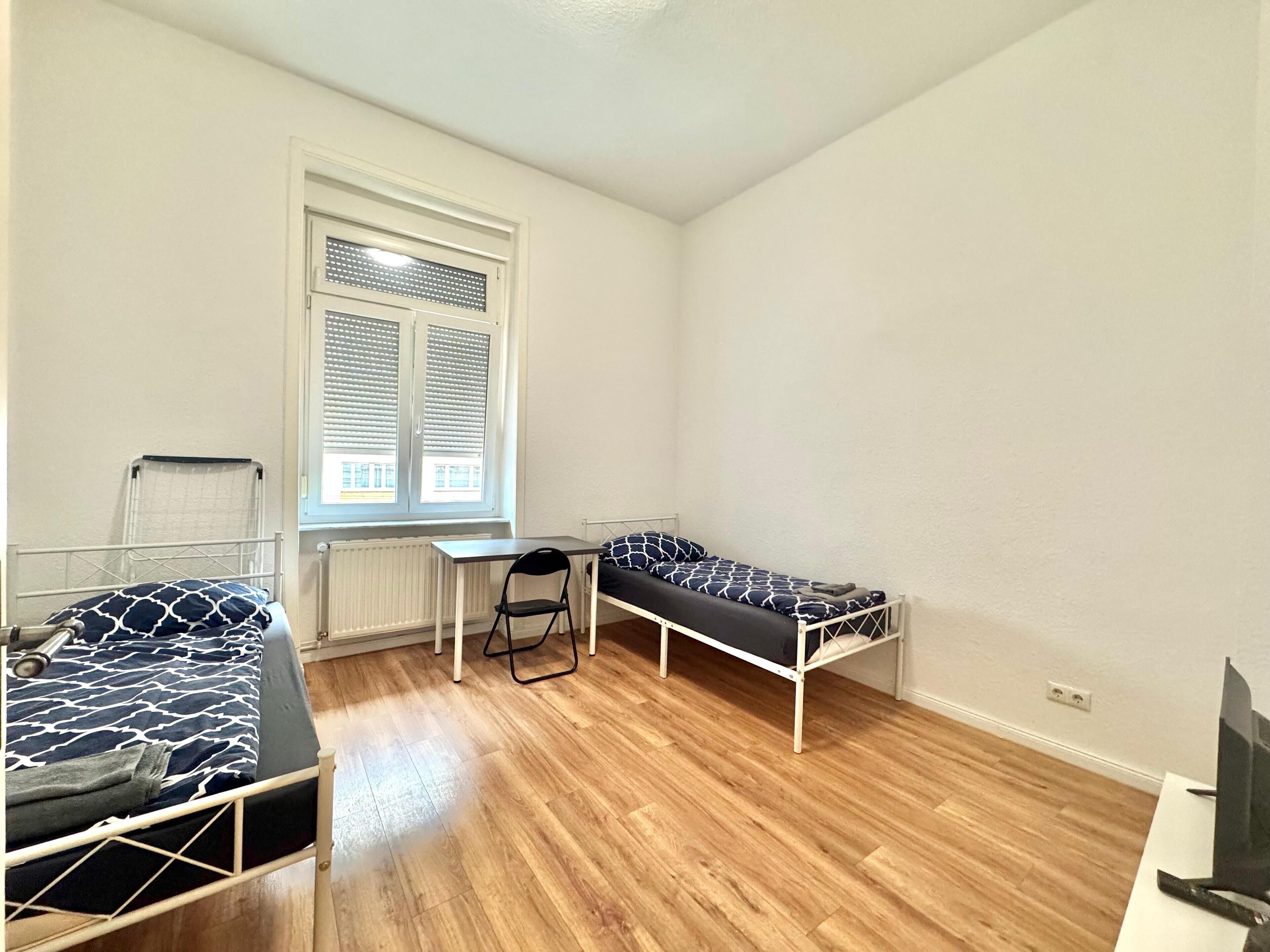 A small room with two beds, a desk, and a chair.