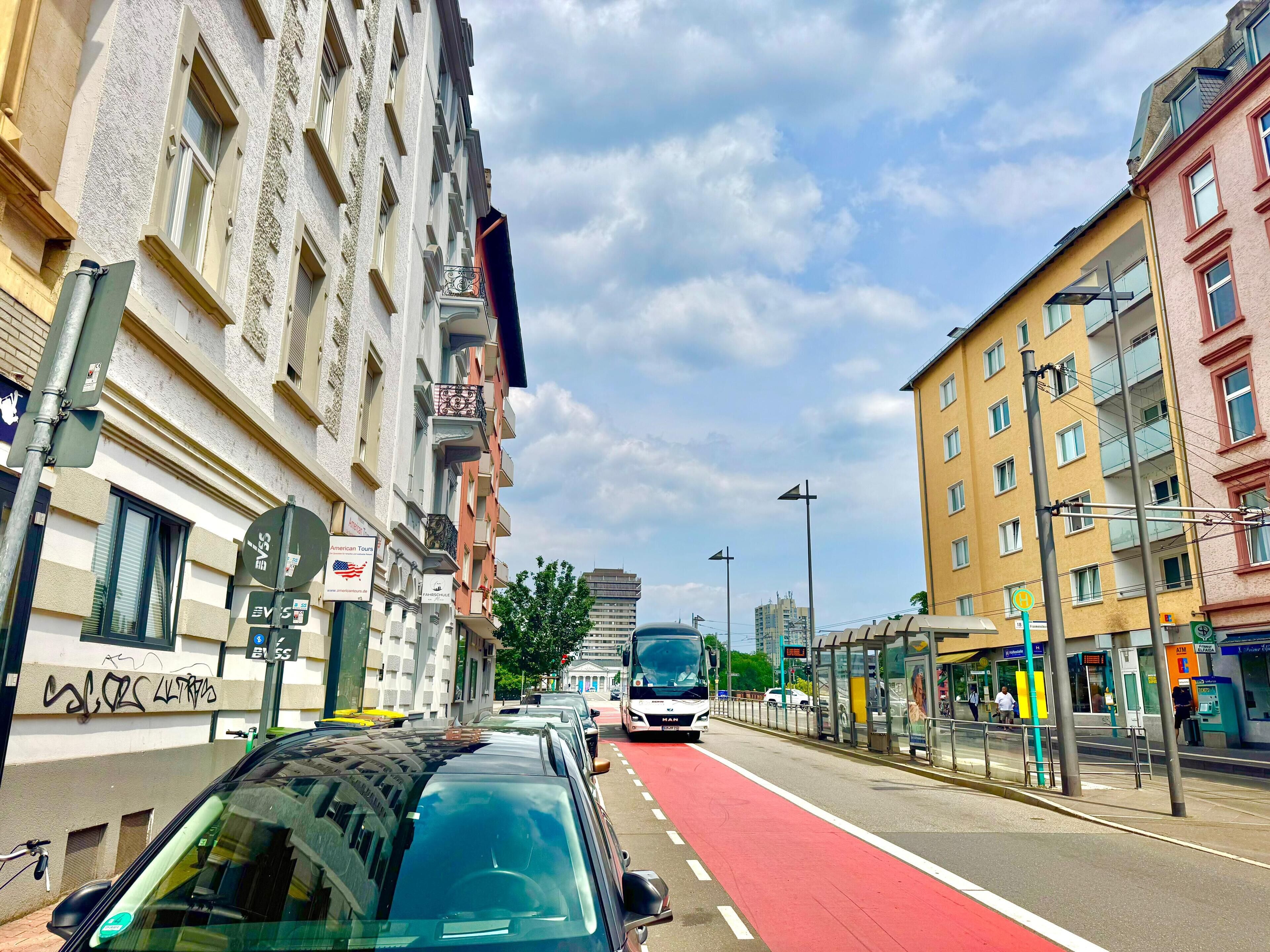 Eine Straße mit roter Fahrradspur, Gebäuden mit Balkonen und einer Bushaltestelle.