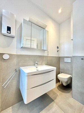 A modern bathroom with a white sink, a mirror, and a toilet. - Family Apartments by Main (Frankfurt)