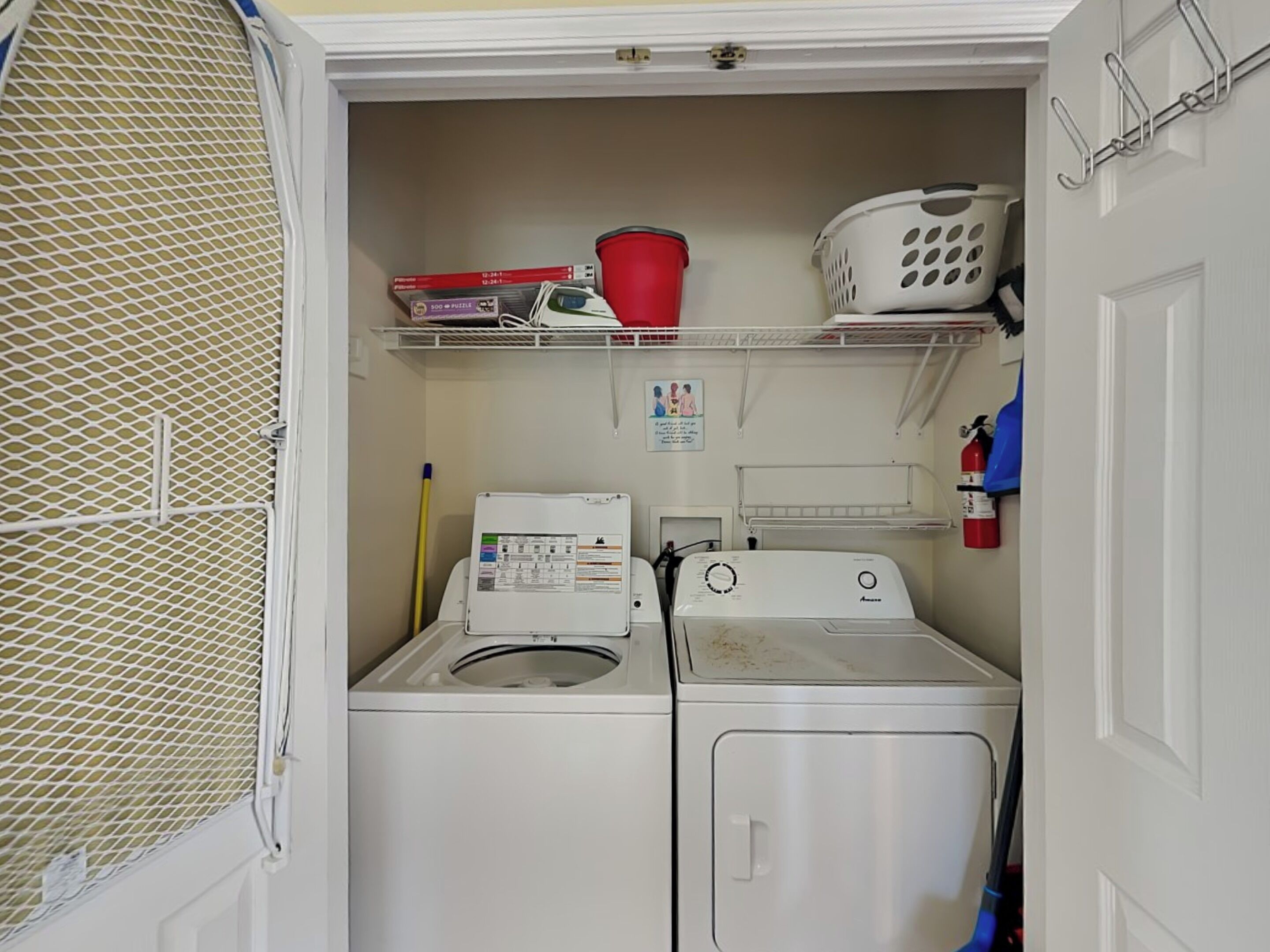 A laundry room with a washing machine, dryer, shelves with laundry baskets, and a fire extinguisher.