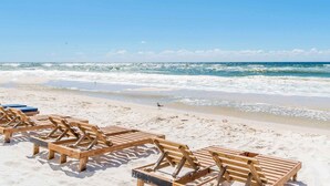 A beach with wooden lounge chairs and a clear view of the ocean. - Crystal Shores #202 by Southern Vacation Rentals (Gulf Shores)
