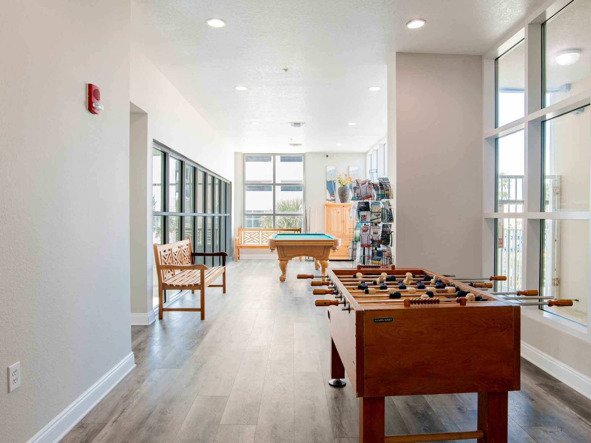 A spacious indoor area with a foosball table, a pool table, and a seating area with chairs.