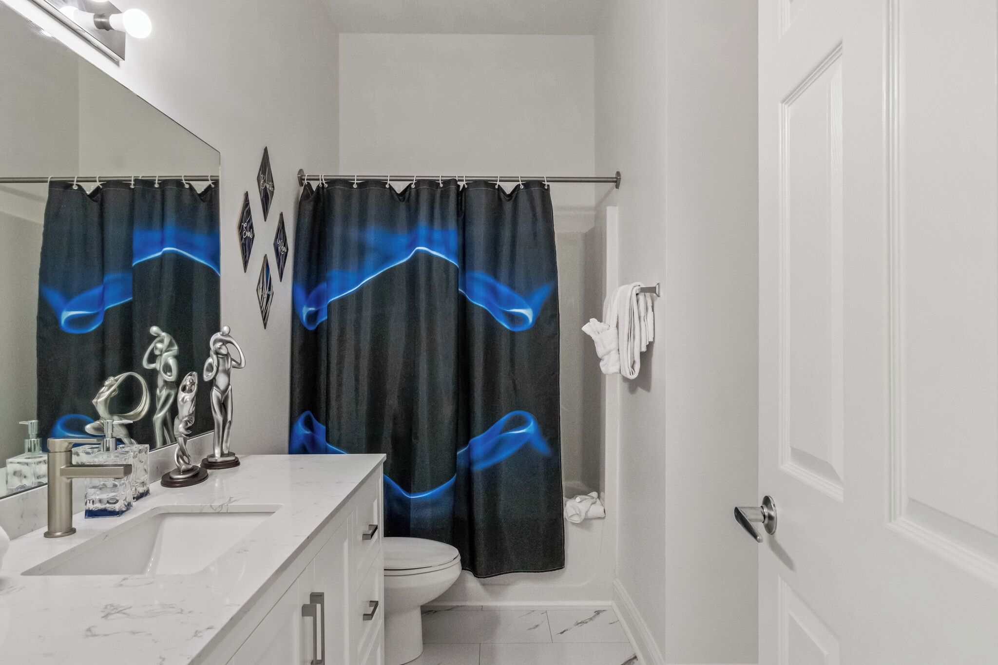 A bathroom with a white sink, a mirror, a toilet, and a shower curtain with blue patterns.