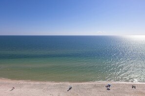 A beach with clear water and a few people walking along the shore. - Crystal Shores West #501 by Southern Vacation Rentals (Gulf Shores)
