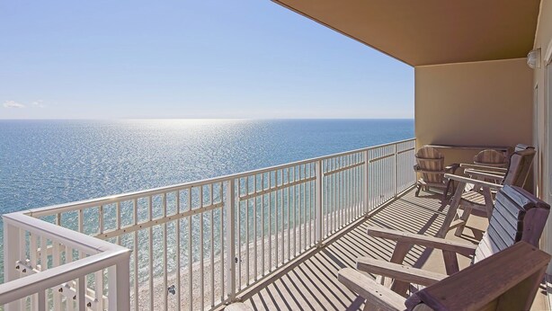 A balcony with a view of the ocean, wooden furniture, and a white railing.