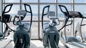 A fitness room with stationary bikes and treadmills, large windows with a beach view.