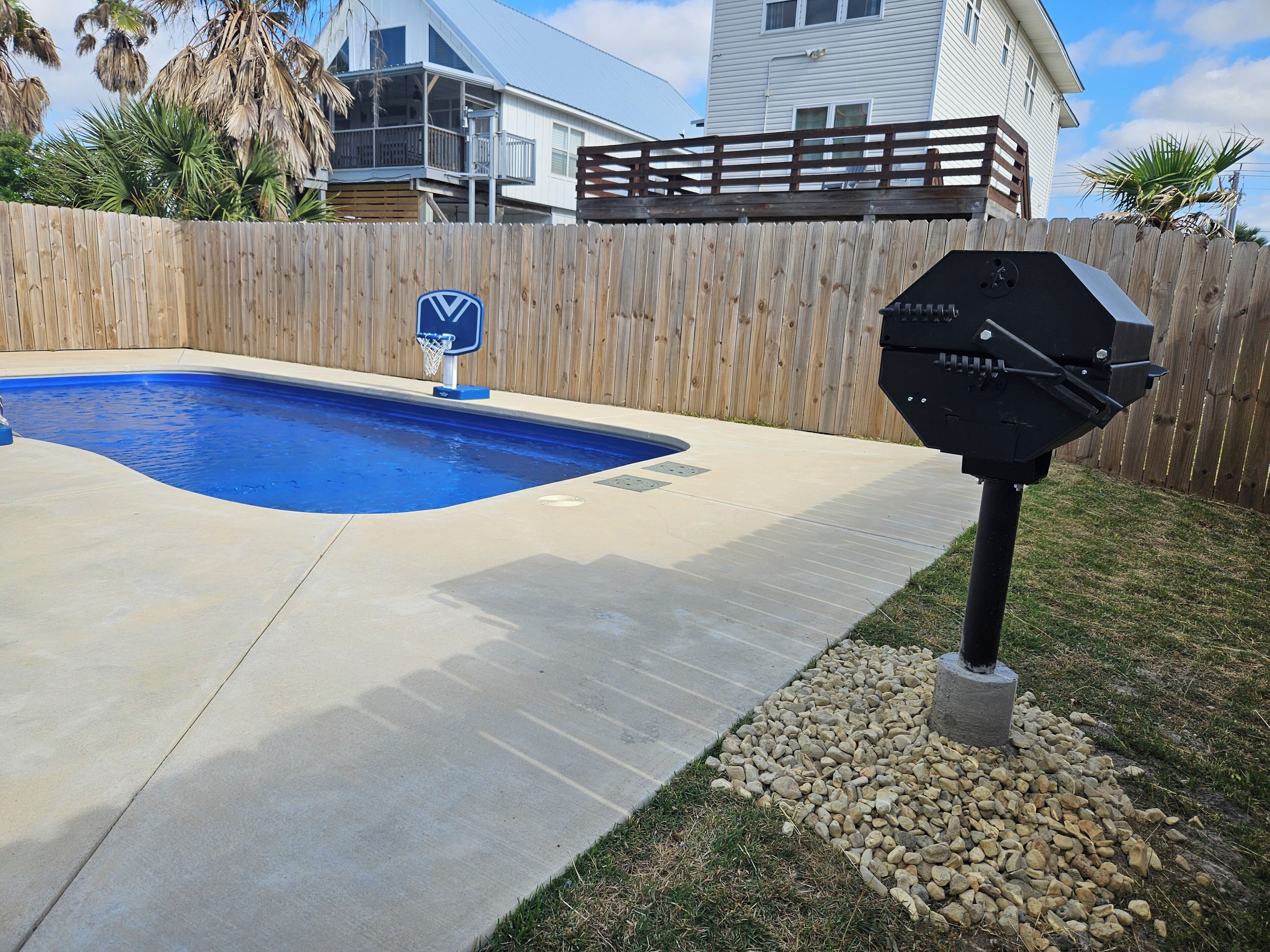 A backyard with a swimming pool, a barbecue grill, and a wooden fence.