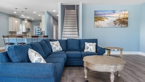 A modern living room with a sectional sofa, a wooden coffee table, and a painting of a beach scene.