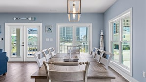 A dining room with a large wooden table, white chairs, and a chandelier.