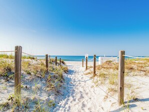 Ein Sandweg am Strand, der zum Meer führt, mit Holzpfählen und Seilen markiert.