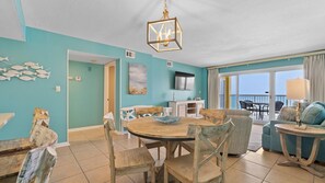 A room with teal walls, a wooden dining table, and a view of the ocean through large windows. - Driftwood Towers #4E by Southern Vacation Rentals (Gulf Shores)
