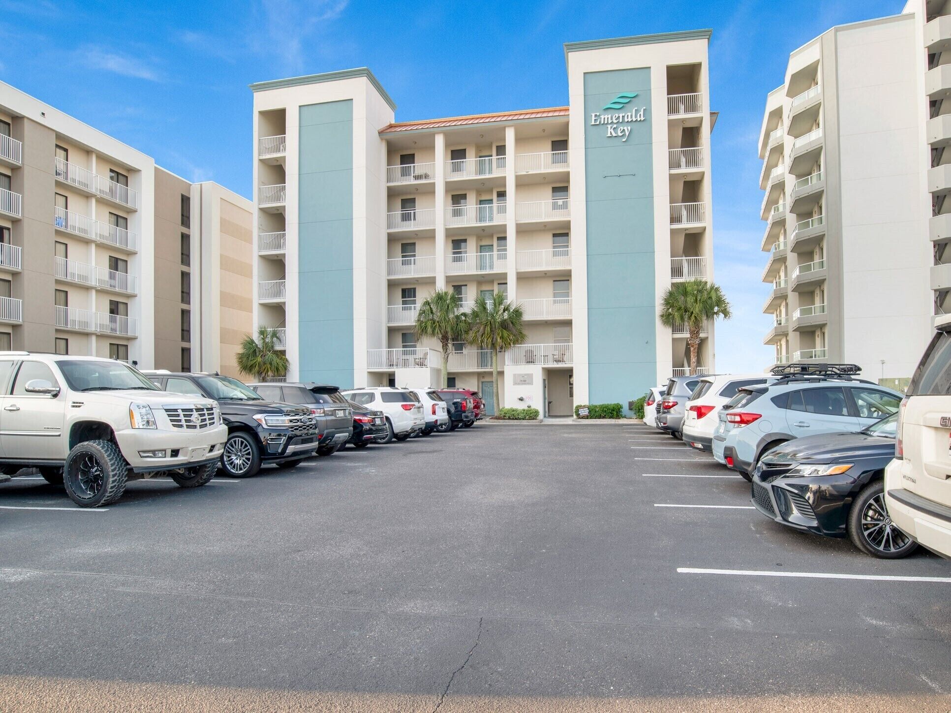 A parking lot with multiple SUVs and cars parked in front of a hotel named Emerald Key.
