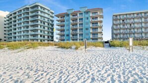 Et hotel ved stranden med flere etager, balkoner og en sandstrand i forgrunden.