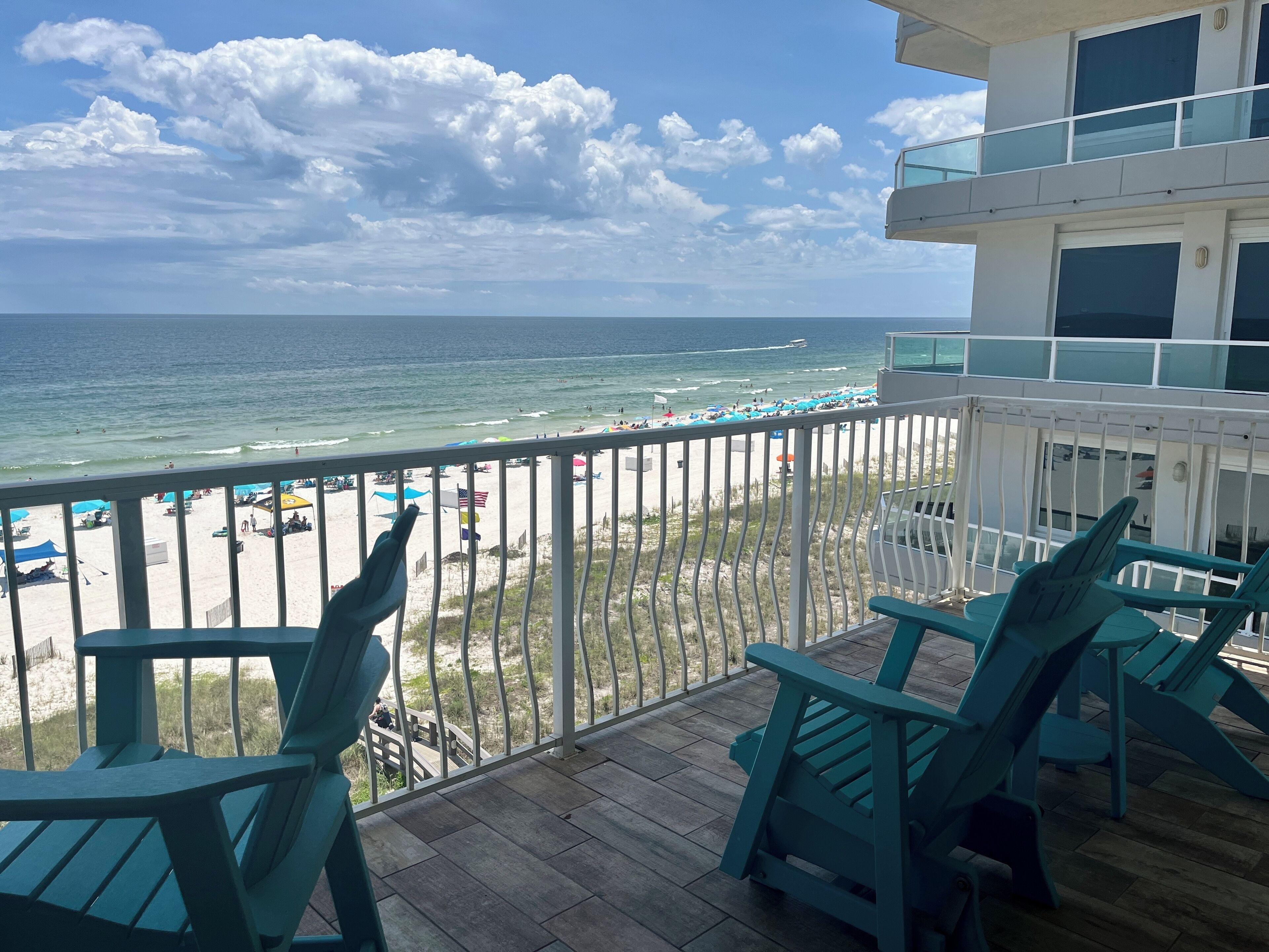 A balcony with a view of a beach and ocean. There are chairs and a railing.