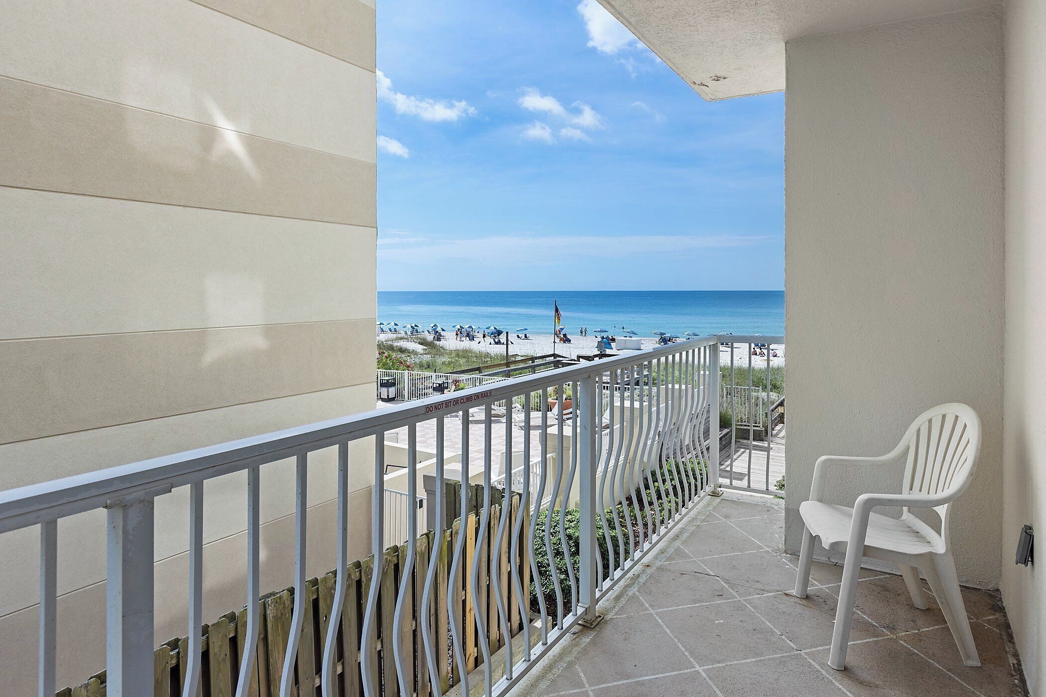 Un balcon donnant sur la plage, une chaise blanche et une balustrade.