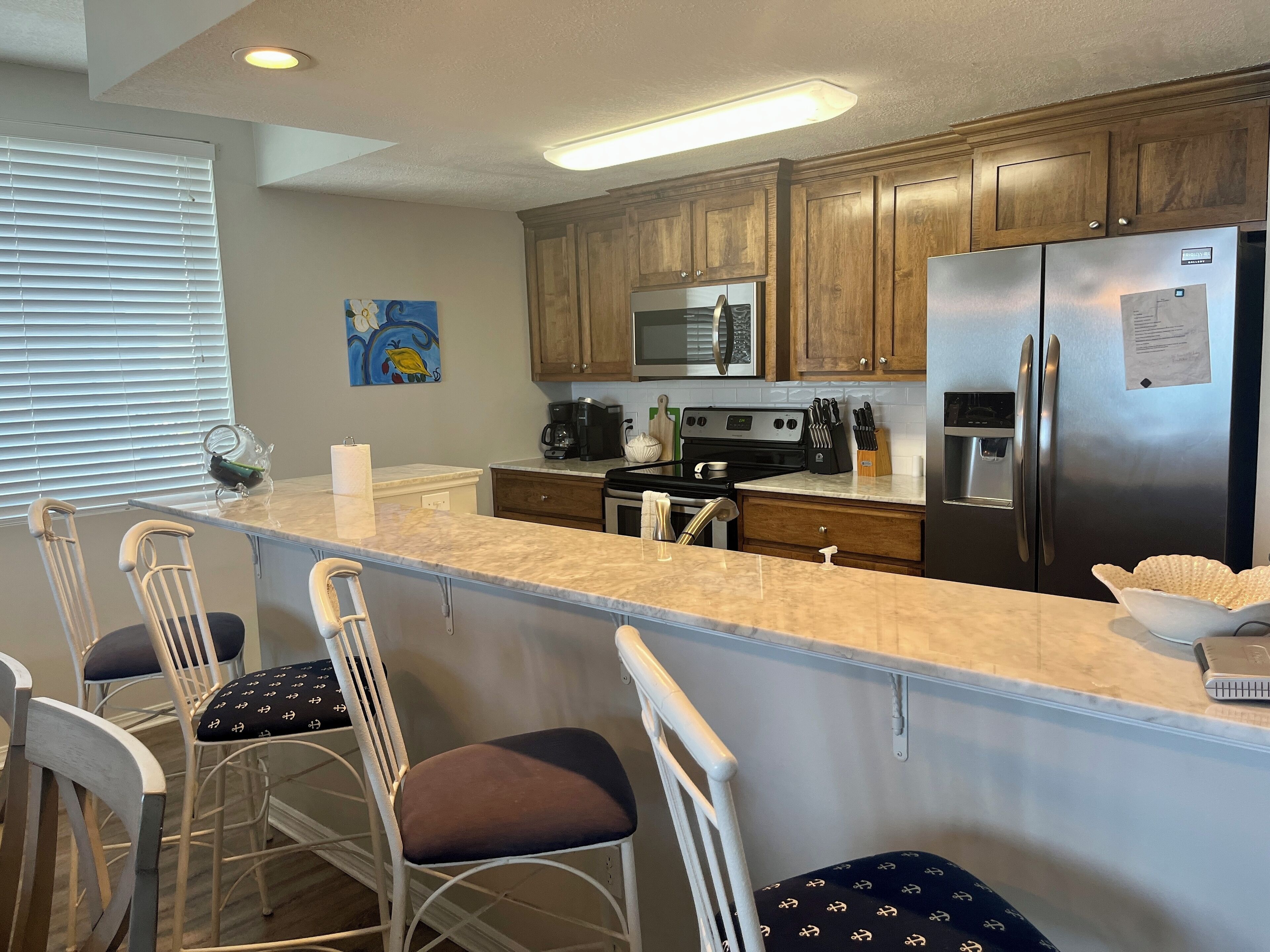 A kitchen with wooden cabinets, stainless steel appliances, a marble countertop, and bar stools.