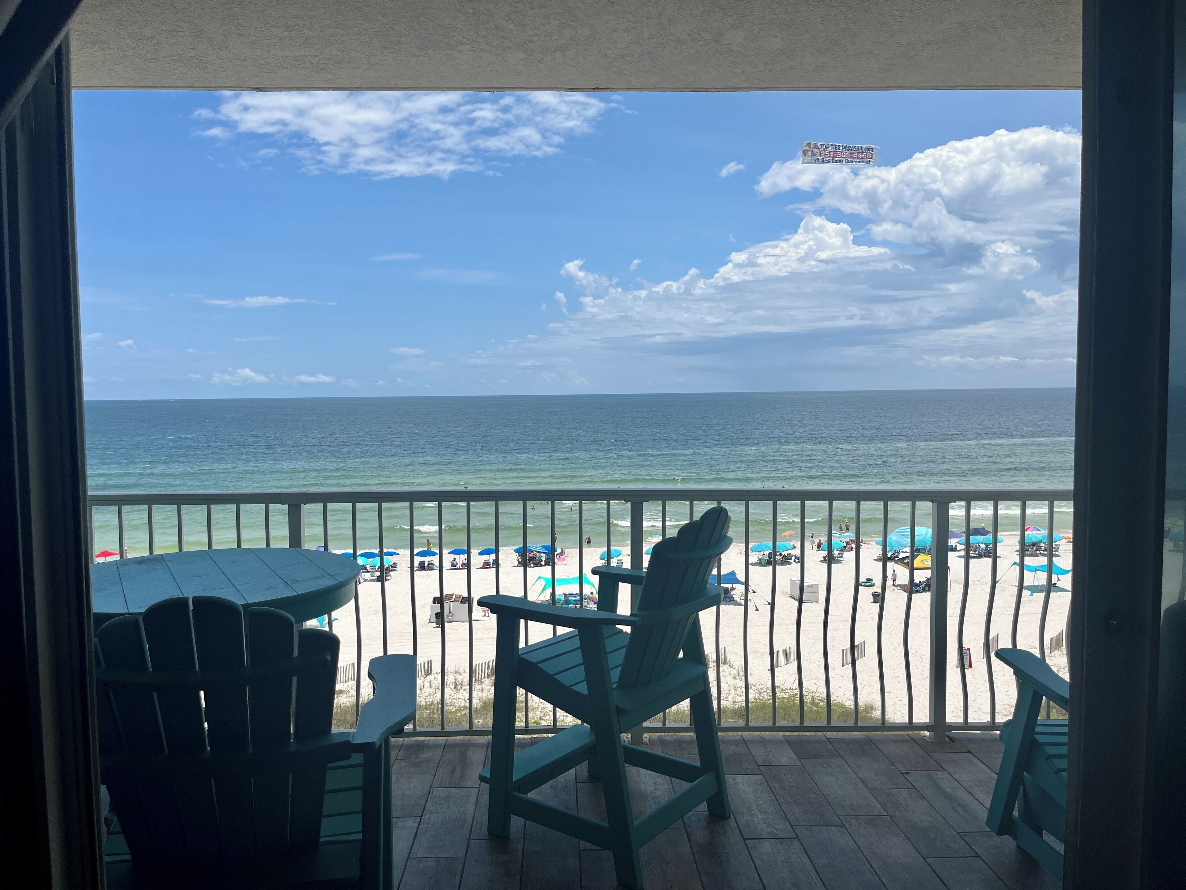 A balcony with a view of the beach, featuring a railing, a table, and two chairs.