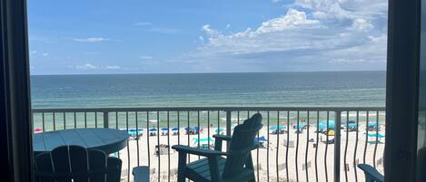 A balcony with a view of the beach, featuring a railing, a table, and two chairs.