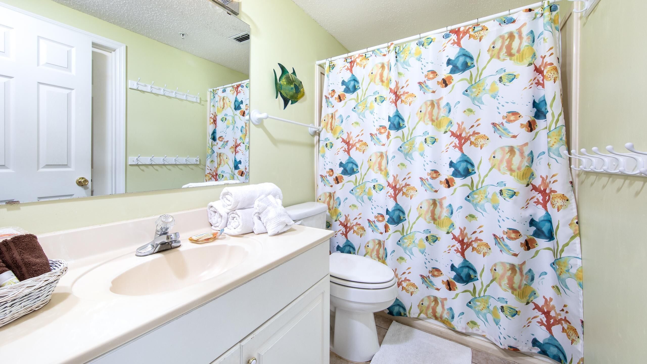 A bathroom with a white sink, a toilet, and a shower curtain with a fish pattern.