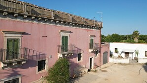 A pink building with balconies, a small garden, and a white building in the background.