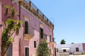 Een roze gebouw met balkons, een kleine boom en een witte structuur op de achtergrond.