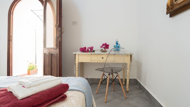 A bedroom with a bed, a desk, and a chair. There is a window with a view of the outside.