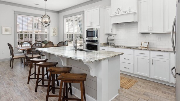 A modern kitchen with white cabinetry, a large island with stools, stainless steel appliances, and a view through the window. - Endless Summer by Southern Vacation Rentals (Orange Beach)