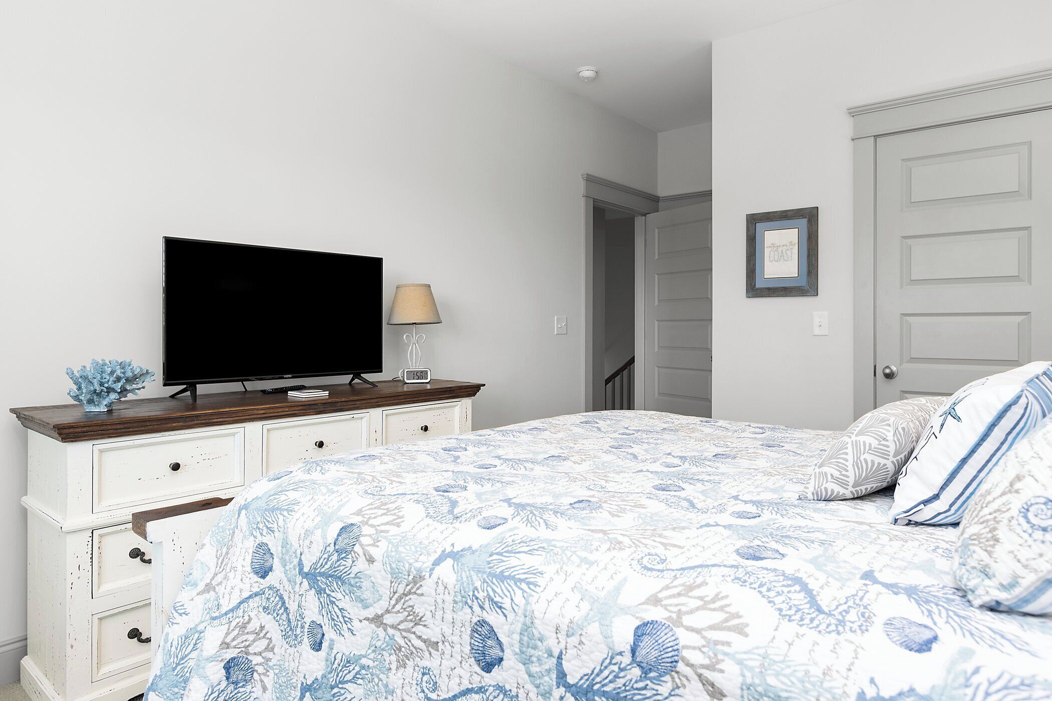 A bedroom with a bed, a TV on a dresser, a lamp, and a door.