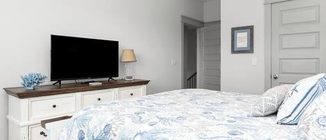 A bedroom with a bed, a TV on a dresser, a lamp, and a door.