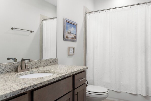 Une salle de bain avec un lavabo à vasque en granit, un miroir, un tableau encadré et un rideau de douche blanc.