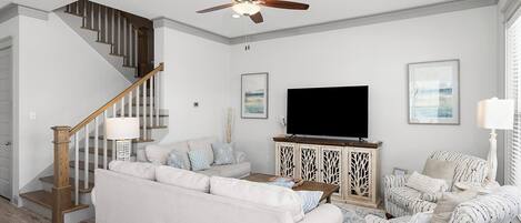 A living room with a staircase, a ceiling fan, a flat-screen TV, and a patterned armchair.