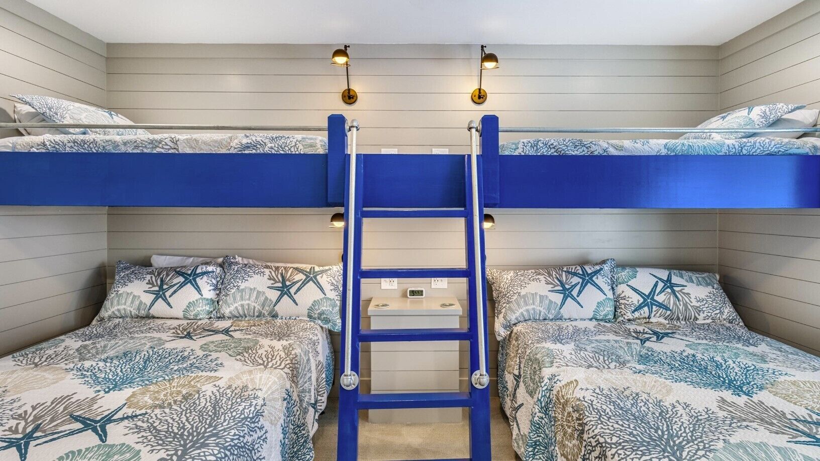 A bunk bed room with a ladder, two beds with starfish and coral patterns, and a shelf with a clock.