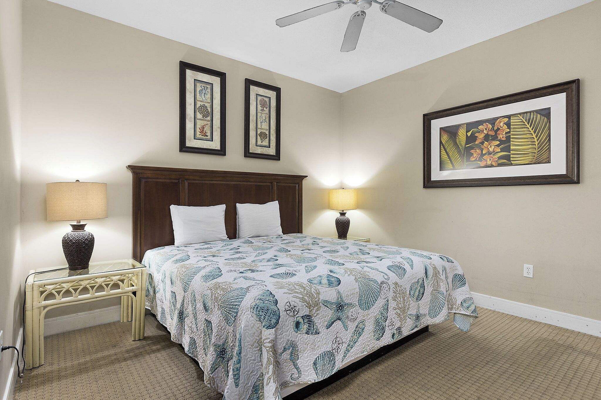 A bedroom with a bed, two bedside lamps, a ceiling fan, and framed artwork on the walls.