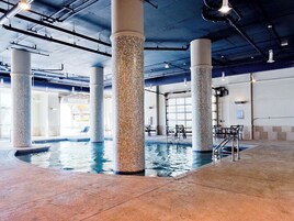 An indoor swimming pool with tiled columns and a tiled floor, surrounded by chairs and tables.
