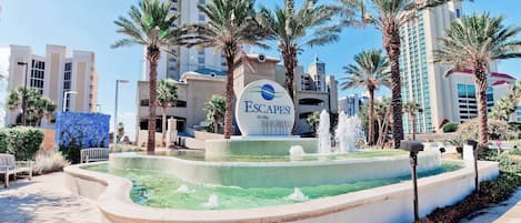 A hotel entrance with a sign reading 'Escapes! To The Shores' and a fountain in the foreground.