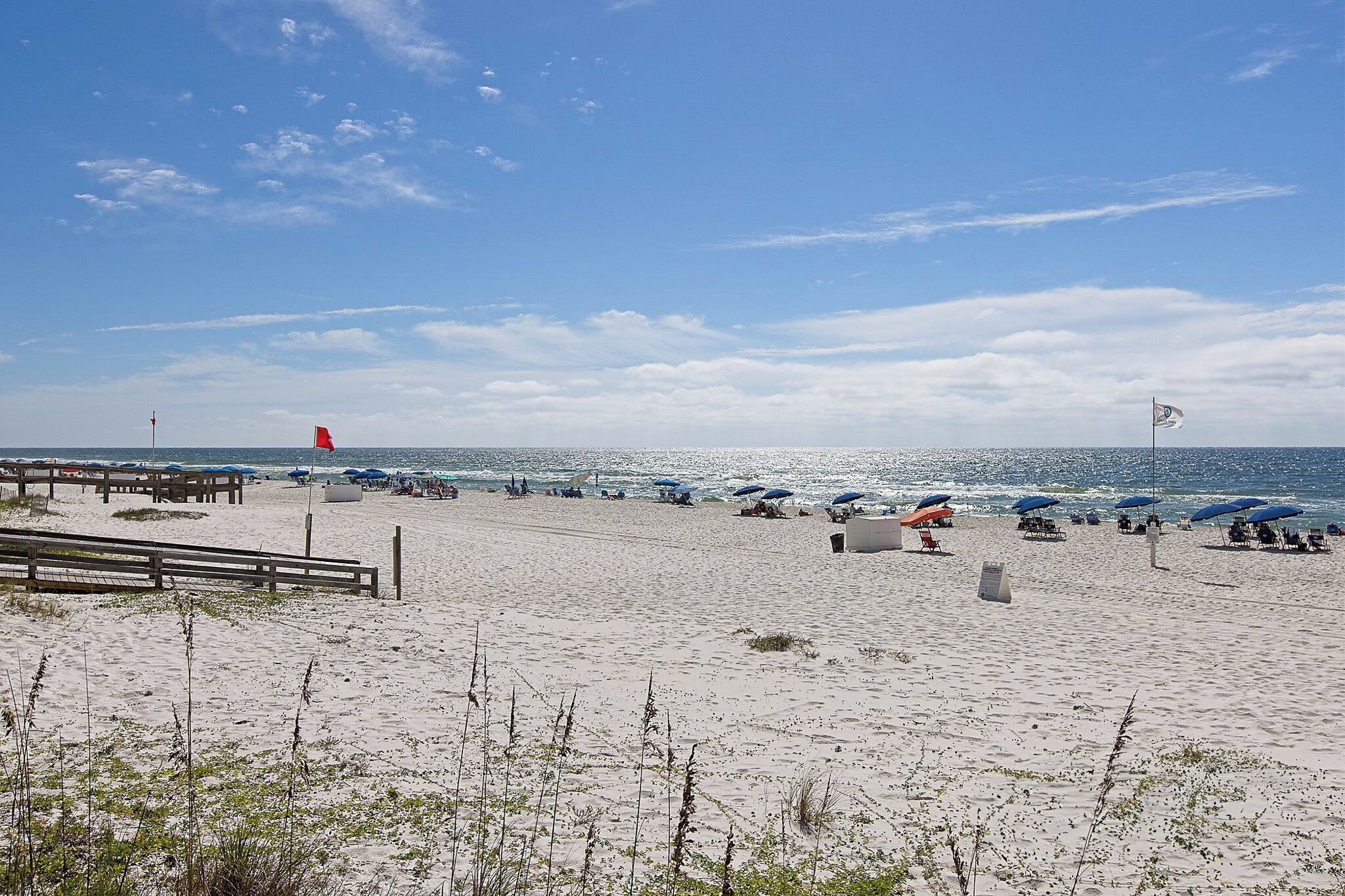 A beach with umbrellas and lounge chairs, a lifeguard tower, and a flag.