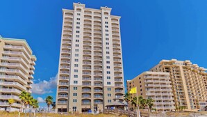 Ein Hotel direkt am Strand mit mehreren Etagen, Balkonen und einem Sandstrand im Vordergrund.