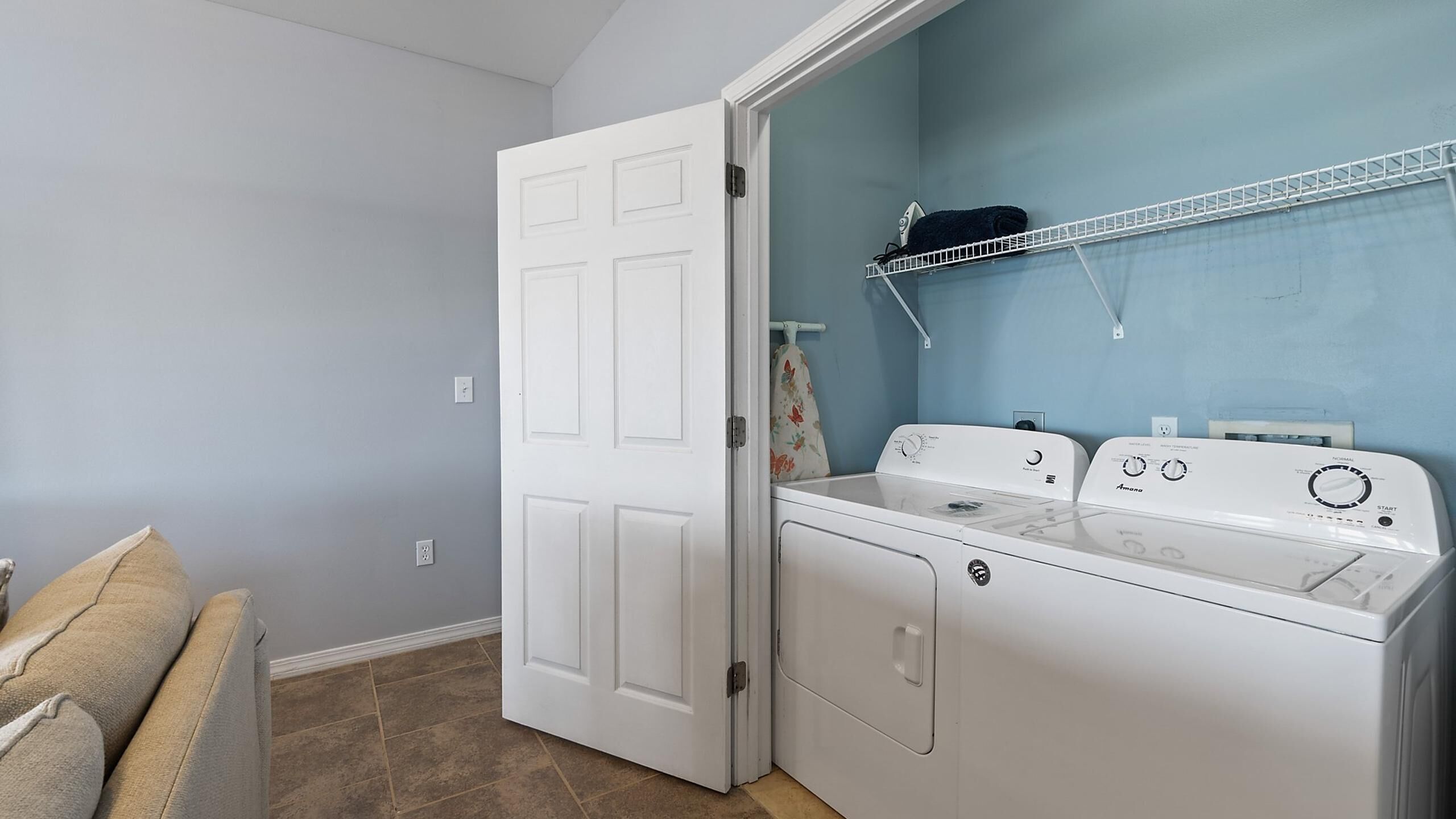 A laundry room with a front-loading washer and dryer, a drying rack, and a door leading to another room.