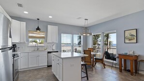 A modern kitchen with white cabinets, a central island, and a dining area with a view. - Flip Flop Bay House by Southern Vacation Rentals (Elberta)