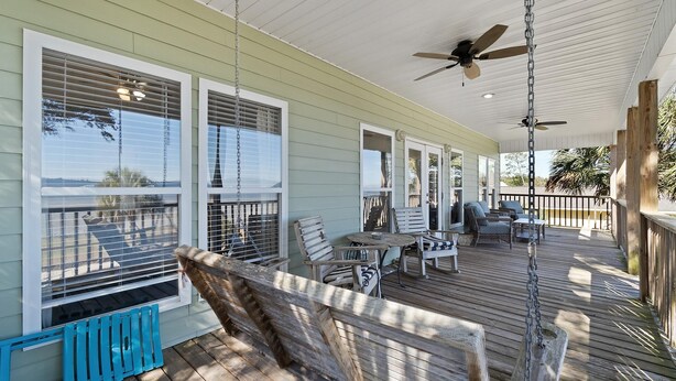 A covered porch with a ceiling fan, wooden deck, and outdoor seating area with chairs and tables. - Flip Flop Bay House by Southern Vacation Rentals (Elberta)