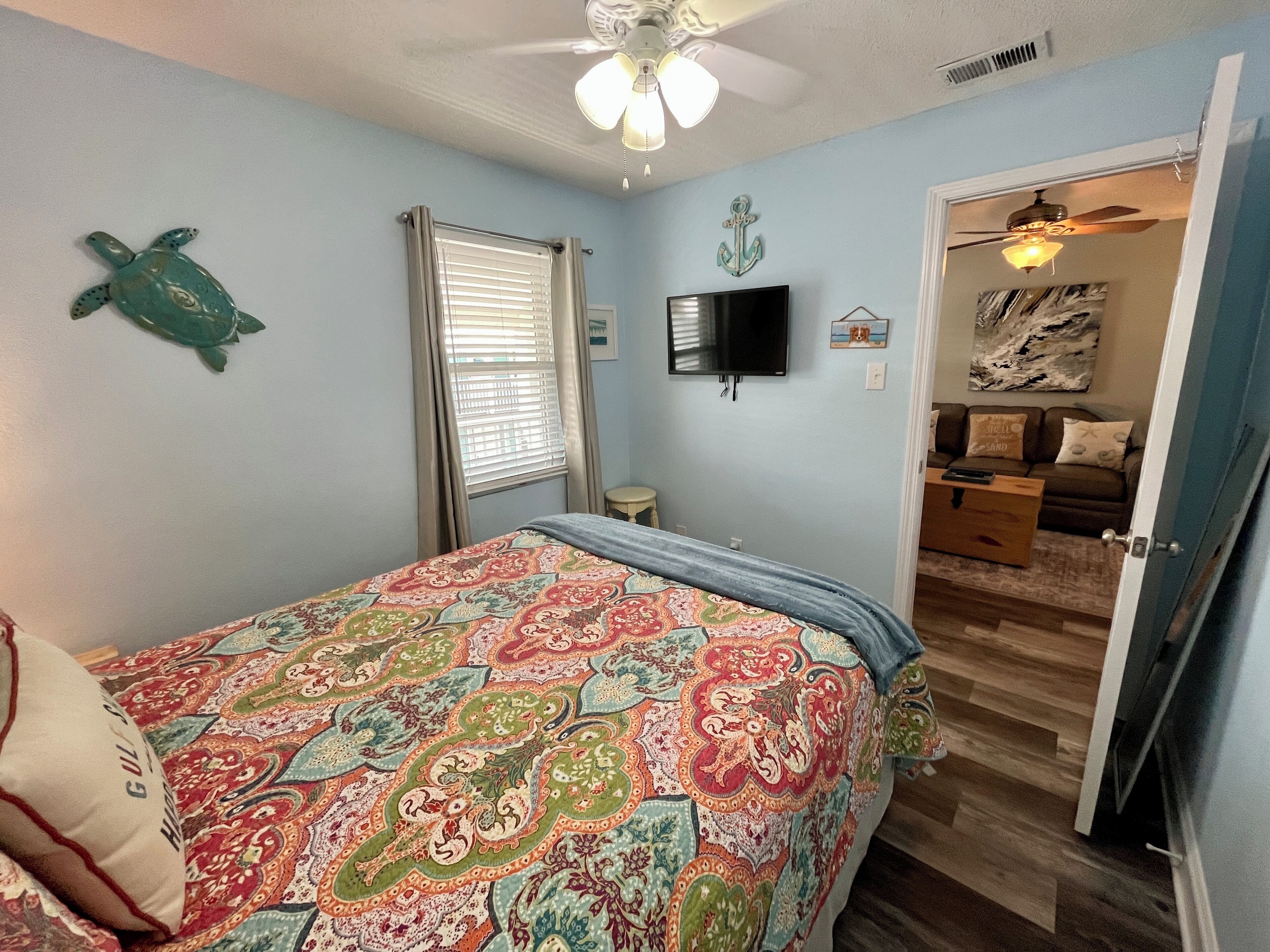 A bedroom with a bed, a ceiling fan, a TV, and a door leading to another room.