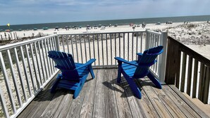 A wooden deck with two blue Adirondack chairs facing a beach. - Sunrise Village #216 by Southern Vacation Rentals (Gulf Shores)