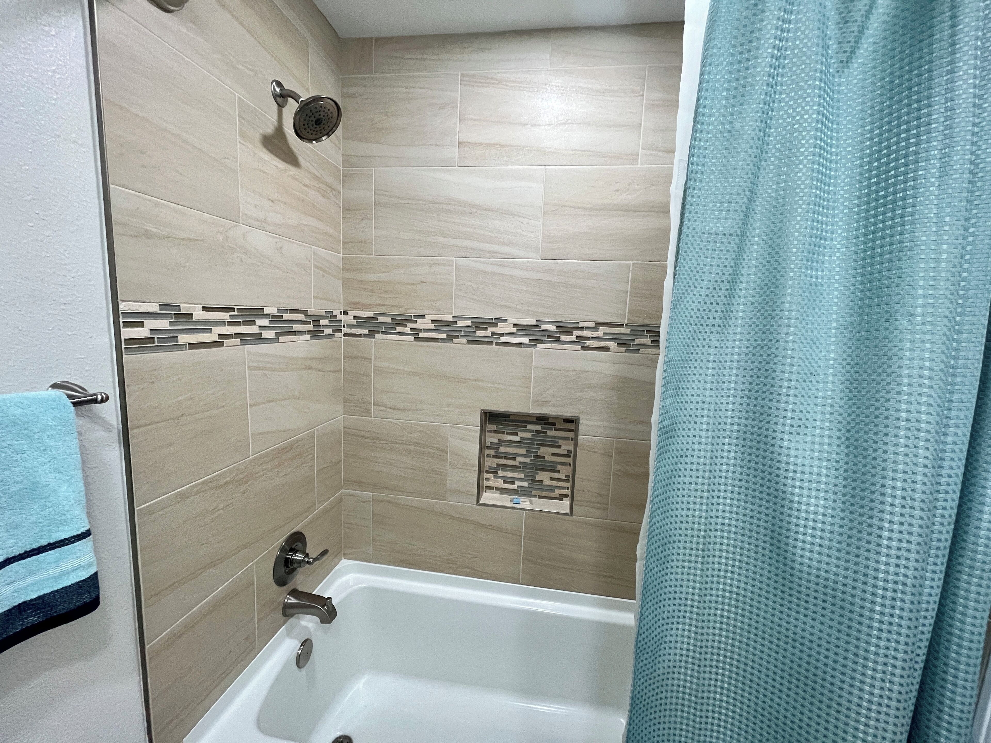Ein Badezimmer mit Badewanne, Duschkopf und einer gefliesten Wand mit dekorativer Bordüre.