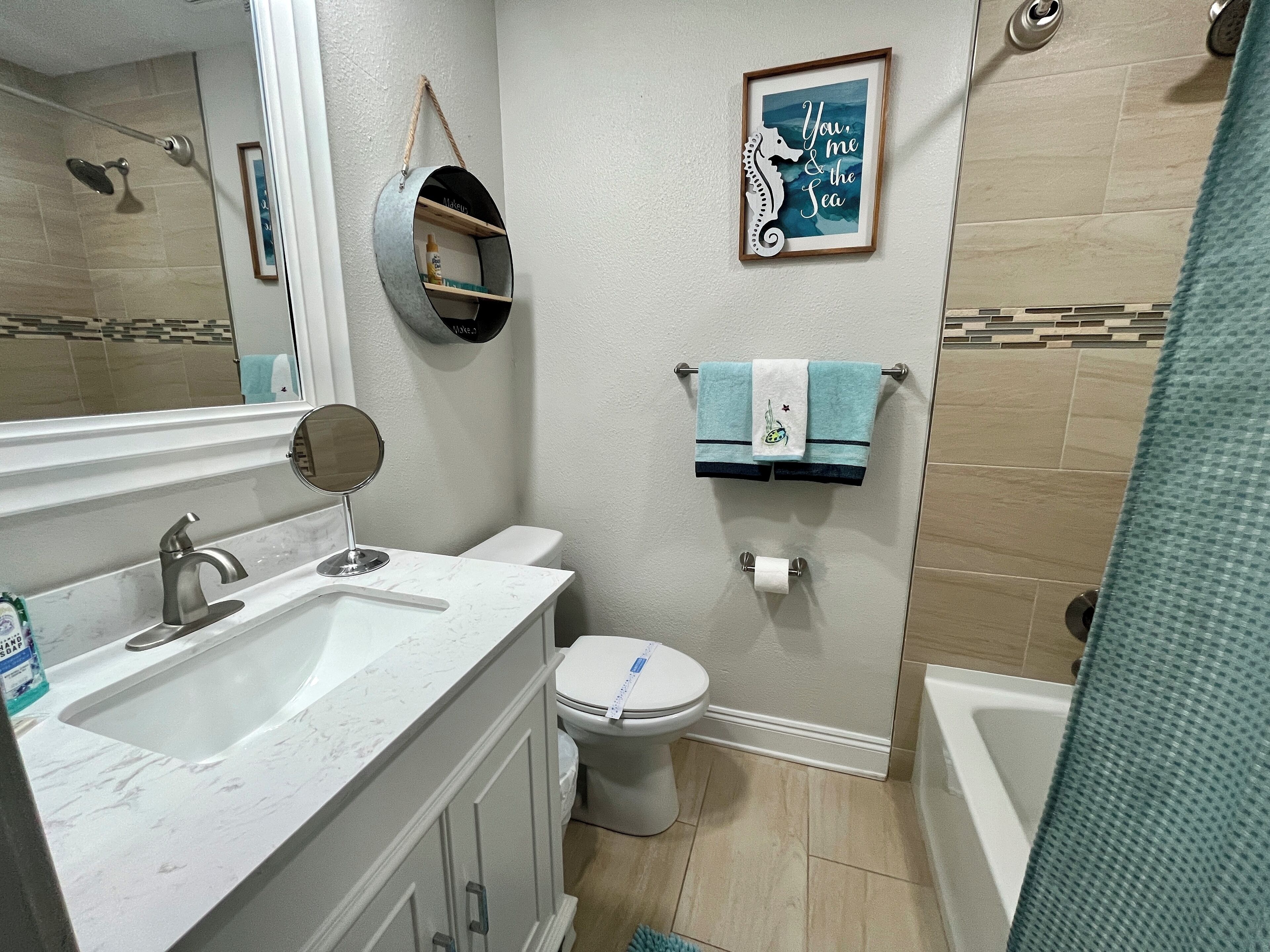 A bathroom with a sink, toilet, and bathtub. There is a towel rack with two towels and a framed quote on the wall.